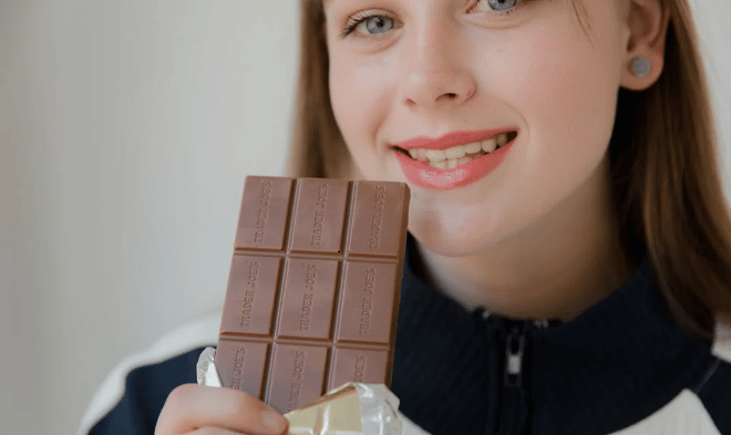 Garota segurando uma barra de chocolate preto e sorrindo