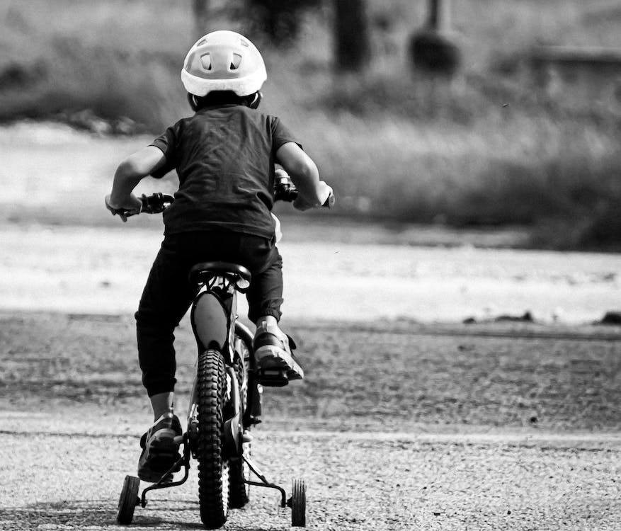 Criança pedala de costas com tela em preto e branco