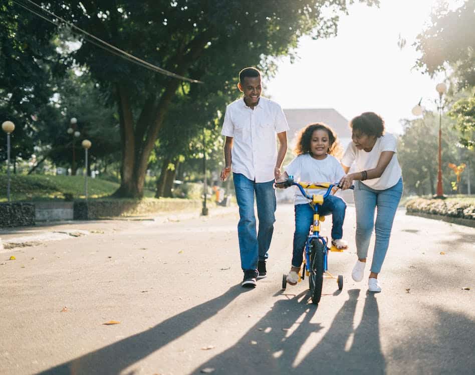 pais brincam com criança que está na bicicleta infantil