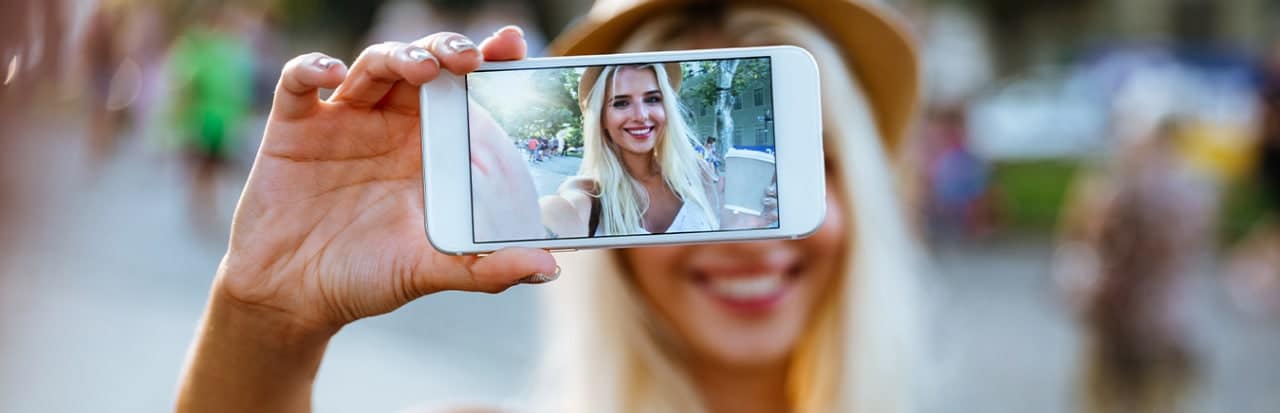 Mulher loira com celular na mão tirando uma selfie