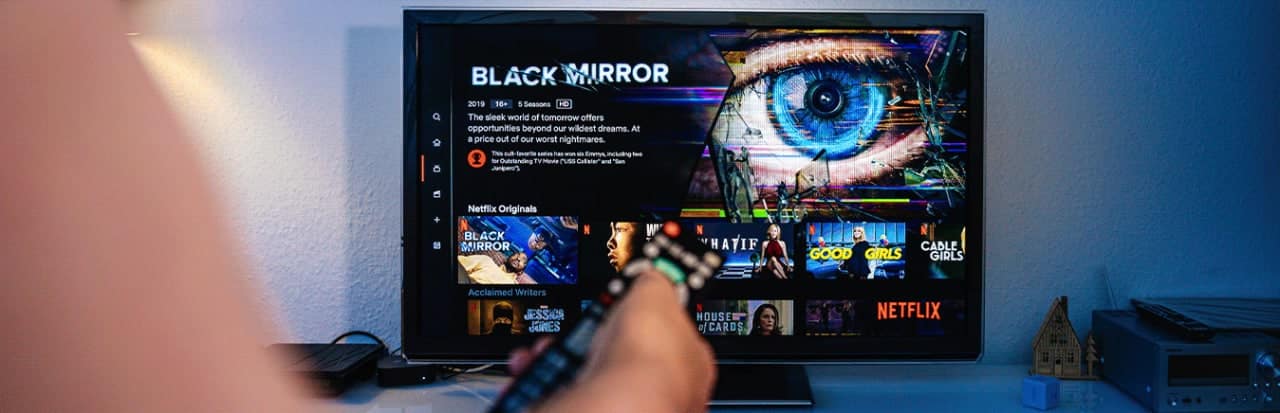 Pessoa com controle remoto na mão apontando para a TV para ver as estreias da netflix