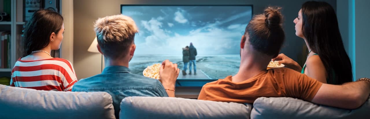 Pessoas comendo pipoca de frente para a TV assistindo filme