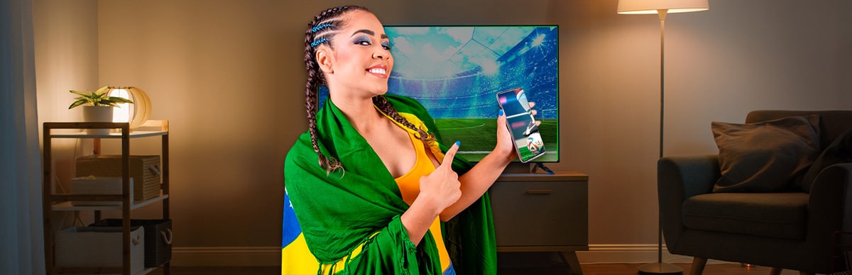 Mulher vestida como torcedora do Brasil segura celular com futebol na tela