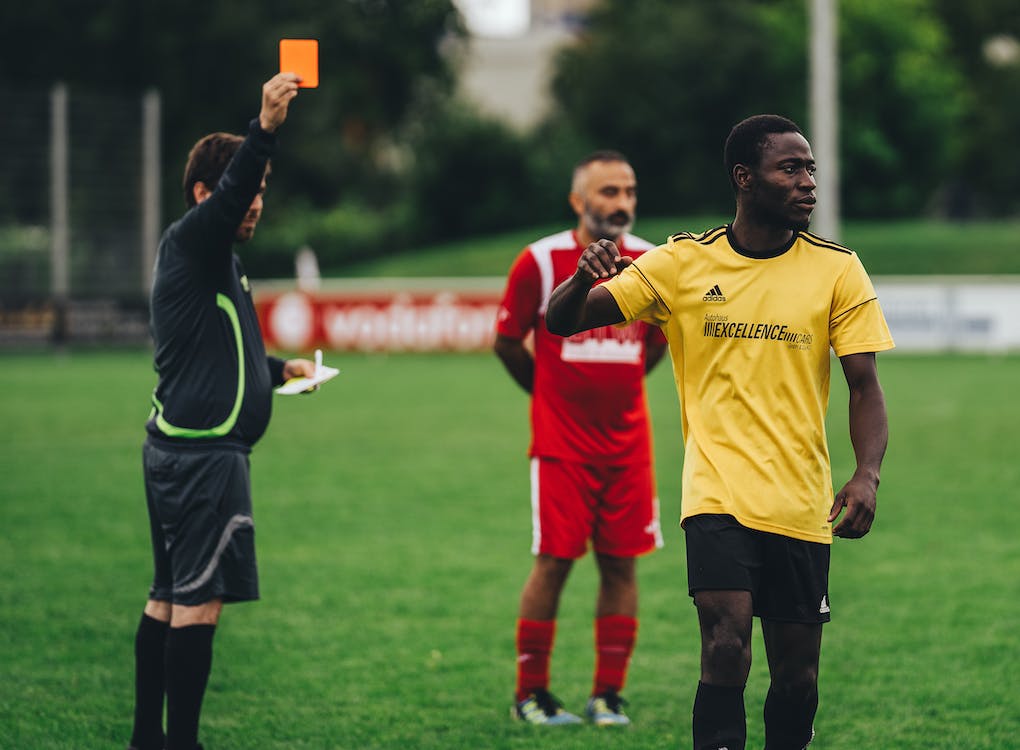 árbitro de jogo de futebol aponta cartão vermelho para jogador em campo